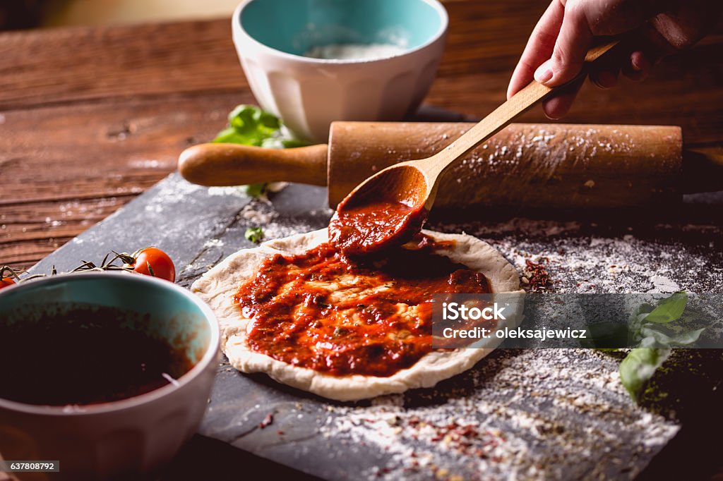 Une fille place de la sauce tomate sur une pizza fraîche - Photo de Pizza libre de droits