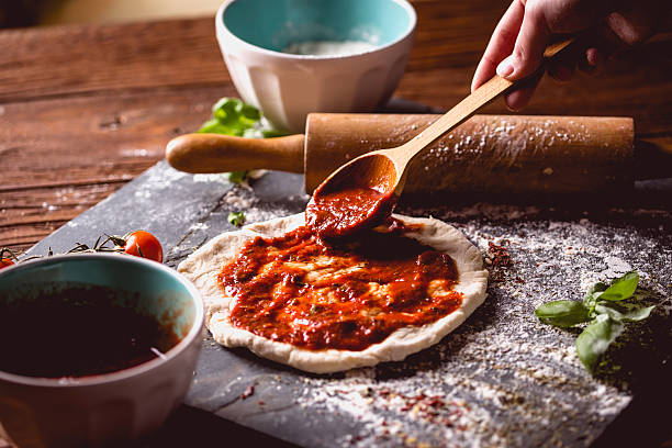 la ragazza sta mettendo la salsa di pomodoro sulla pizza fresca - sugo pronto foto e immagini stock