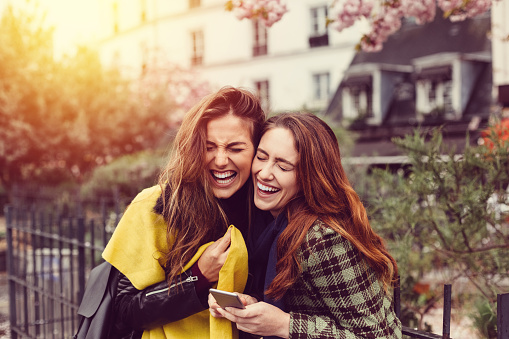 Young women using smartphone and laughing outside
