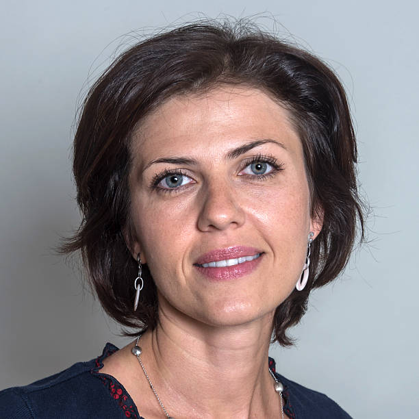 Smiling, Mature Businesswoman:A portrait of a smiling, mature businesswoman from the neck up. She has blue eyes and shoulder length brownish-brown hair that is parted down the middle. She wears a dangling earrings, and a soft pink lipstick.