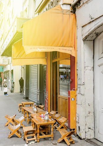 Paris, France - August 18, 2014: Typical Street cafe with chairs on the streets of Paris, France with people talking at the mobile phone in the background