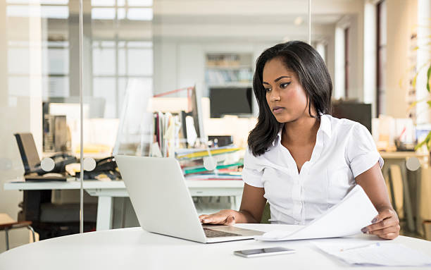 istock Mixed race businesswoman using laptop with documents on desk 637831896