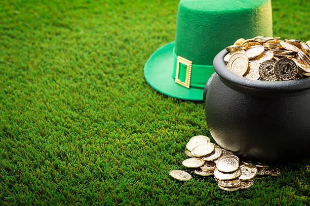 This is a close up photo of a large black pot of gold on the grass with a green hat symbolizing St. Patrick's Day.