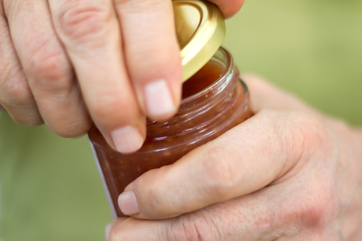 Close-up shot of strong male hands removing lid from glass jar. Green background with copy space.