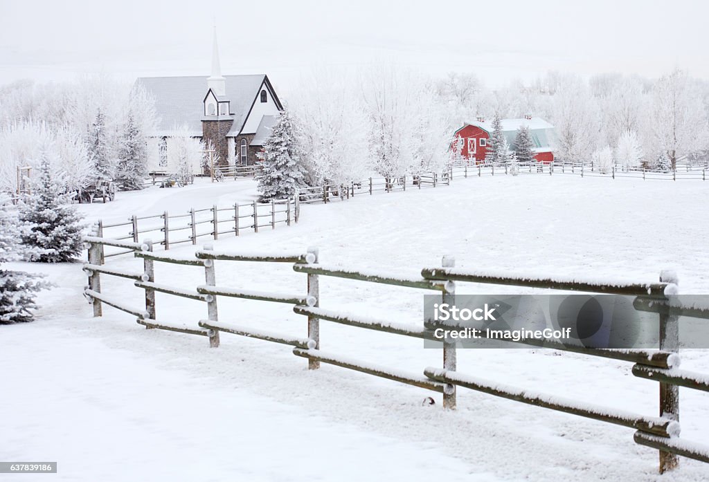 Small Country Church in Winter A little church in the country in winter. Wedding chapel. Alberta, Canada, Rural scenic. Nobody is in the image. A rustic rural scene in a remote village on the great plains. Wooden fence on a farm leads to a quaint white church and red barn. Farm Stock Photo