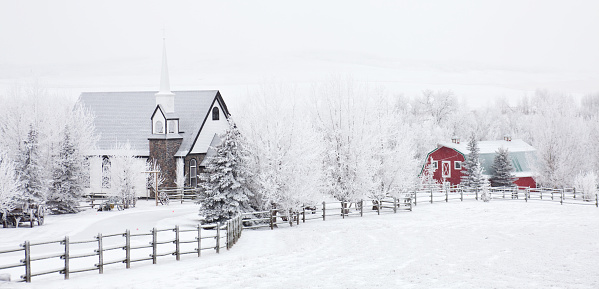 A little church in the country in winter. Wedding chapel. Alberta, Canada, Rural scenic. Nobody is in the image. A rustic rural scene in a remote village on the great plains. Wooden fence on a farm leads to a quaint white church and red barn.