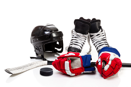 Ice hockey equipment featuring safety helmet, pair of skates, gloves, stick and a hockey puck. Isolated on white background.