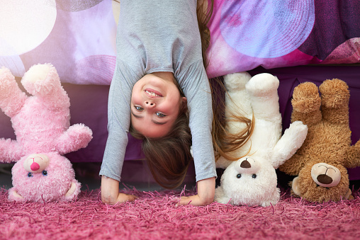 Portrait of a cute little girl doing a handstand in her bedroom at home