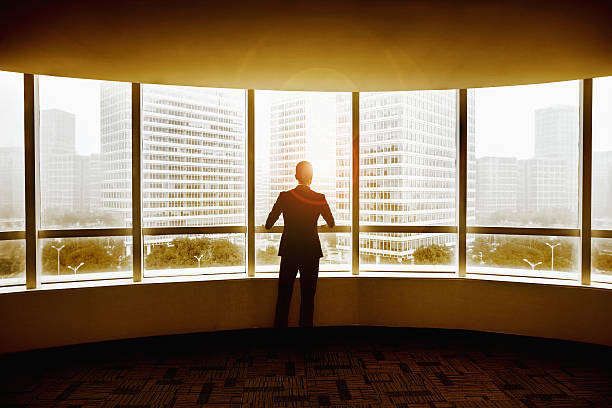 hombre de negocios mirando a la ciudad en la oficina moderna - window sun sunlight vertical fotografías e imágenes de stock