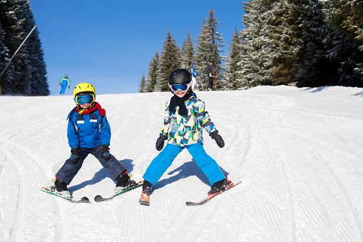 Two young children, siblings brothers, skiing in Austrian mountains on a sunny day, wintertime, enjoying sports