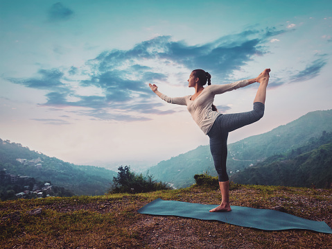 Woman doing yoga asana Natarajasana - Lord of the dance pose outdoors on sunset in Himalayas. Vintage retro effect filtered hipster style image.