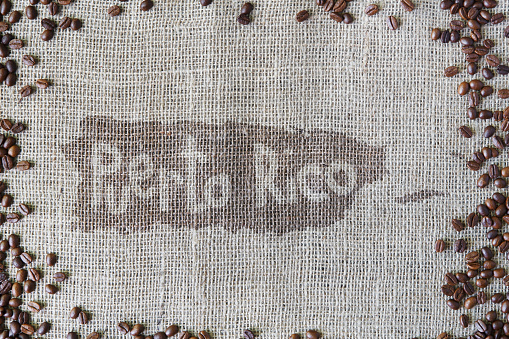 Burlap texture with coffee beans border. Sack cloth background with Puerto Rico title in spot in the middle. Brown natural sackcloth canvas. Seeds at hessian textile