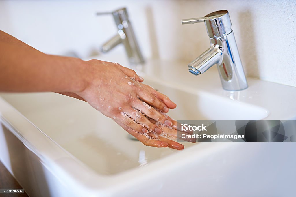 Washing all the germs away A cropped shot of a young woman washing her hands in her bathroom Water Conservation Stock Photo