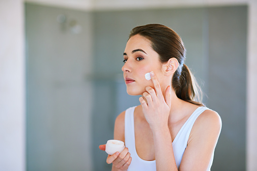 An attractive young woman applying cream to her face