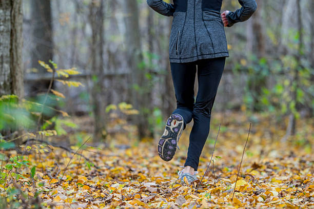 Training for a Marathon A woman is jogging through the woods on an autumn day. spandex stock pictures, royalty-free photos & images