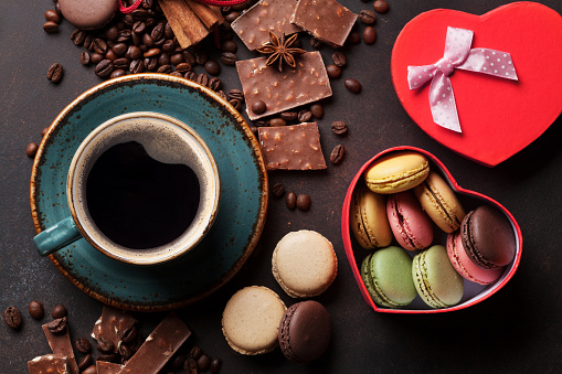 Coffee cup, beans, chocolate, macaroons and gift box on old kitchen table. Top view