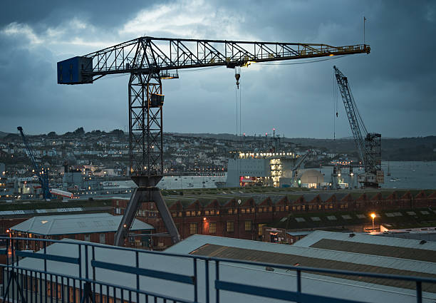 Cranes and buildings at the dockyard in Falmouth Cornwall, early evening in winter as the light begins to fade and the lights come on.  The town of Falmouth and the river Fal estuary are in the background