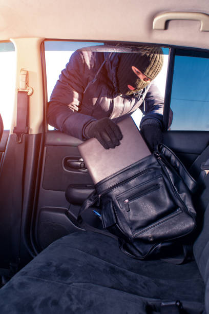istock Thief in robbery mask stealing laptop from car 637892764