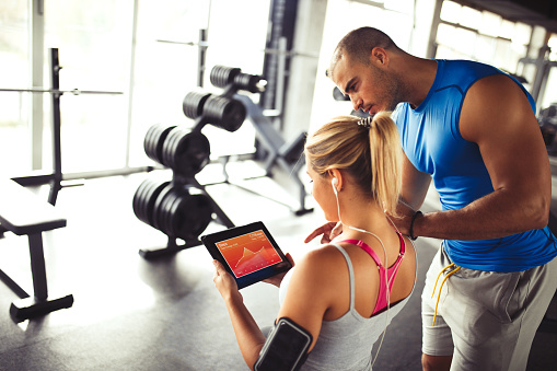 Young sporty woman is  discussing workout plan, progress and statistics with her fitness instructor using digital tablet. Copy space.