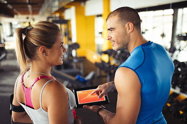 istock Young woman discussing workout progress with fitness instructor 637893696