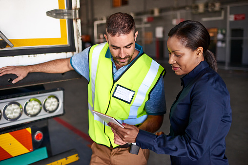 Shot of a manager holding a digital tablet and talking to a truck driver on the loading dock of a large warehouse