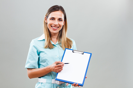 Beautiful nurse is holding clipboard  and showing document with pen.