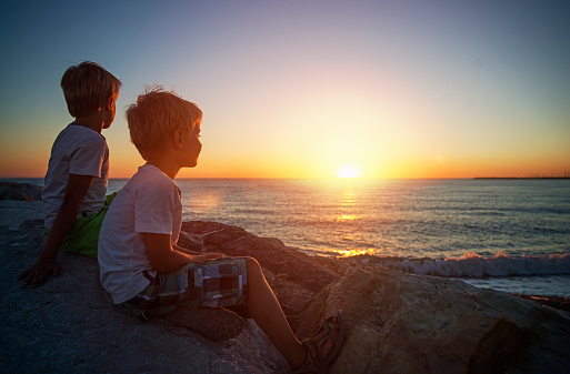Little brothers looking at the sunset over the Italian sea. End of summer vacations. Tuscany, Italy.