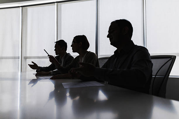 Silhouette of business people negotiating at meeting table Silhouette of business people negotiating at meeting table ominous photos stock pictures, royalty-free photos & images
