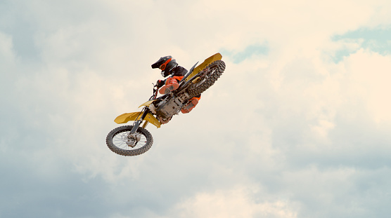 Motocross rider performing stunt in mid-air against cloudy sky.