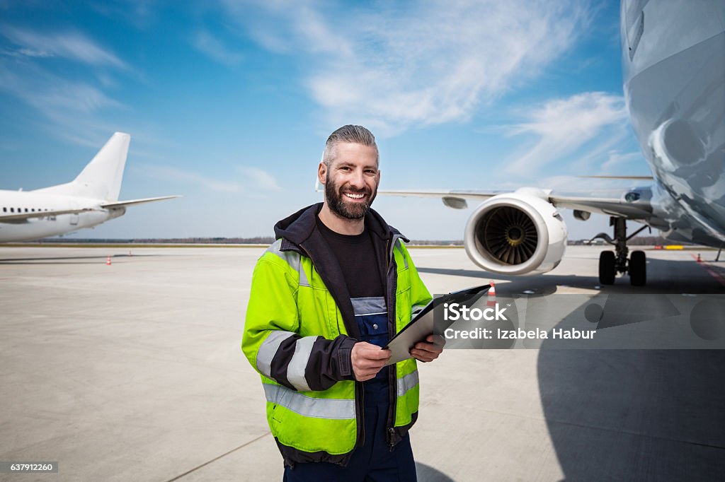 Aircraft worker in front of airplane with checklist Aircraft engineer holding clipboard in hands standing outdoor in front of airplane, smiling at camera. Airport Stock Photo