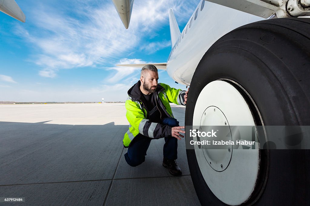 Airport worker checking tires Airport worker chcecking aircraft chassis. Close up. Airport Stock Photo