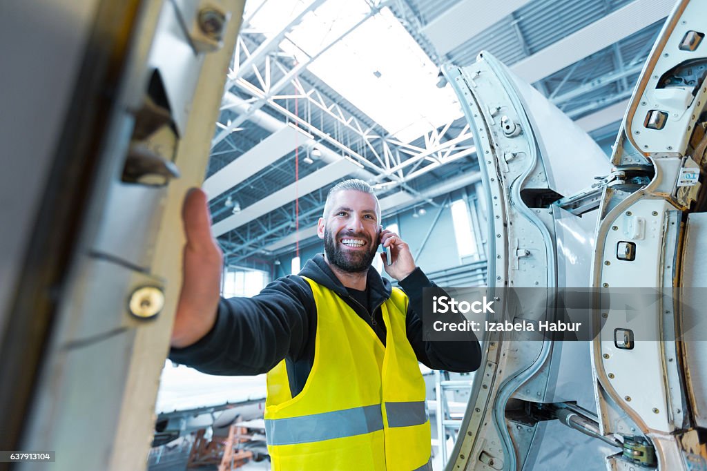 Aircraft engineer talking on smart phone in a hangar Aircraft engineer talking on smart phone in a hangar.  Airplane Mechanic Stock Photo