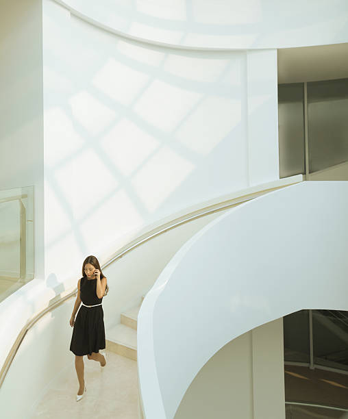 Woman on phone descending staircase in modern building Woman on phone descending staircase in modern building symmetry photos stock pictures, royalty-free photos & images