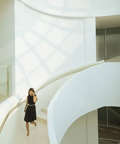 Photo of Woman on phone descending staircase in modern building