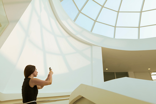 Woman taking photo of modern skylight in atrium
