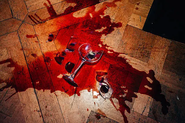 Broken glasses of red wine splashed on hardwood parquet floor
