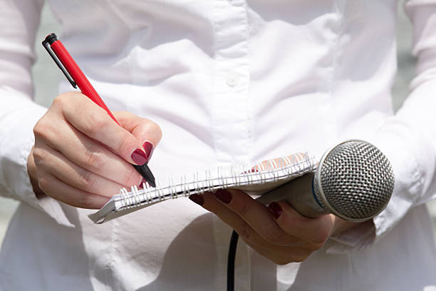 istock Female journalist at news conference, writing notes, holding microphone 637921832