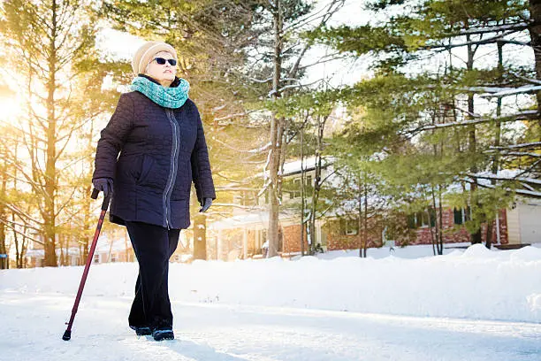 Senior woman enjoying walk with a cane in a Winter suburban scene.