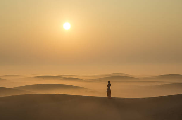 a woman in a desert at sunrise near Dubai stock photo