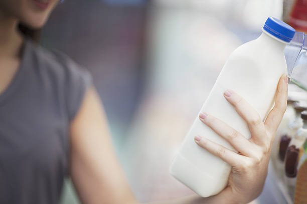 woman checking label on milk in supermarket dairy section - milk milk bottle dairy product bottle imagens e fotografias de stock