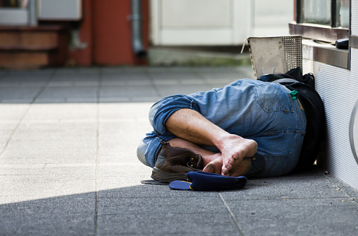 Homeless. Homeless man sleeps on the street, in the shadow of the building. Social documentary.