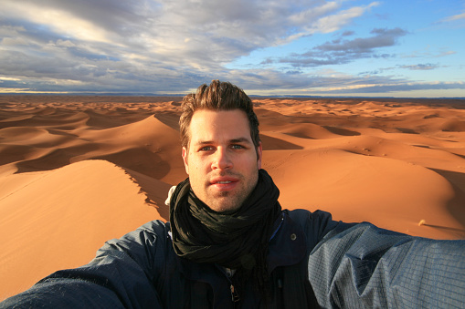 Male solo traveler taking selfie at dunes in Sahara desert, Morocco.