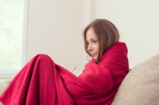 Young woman sitting on a couch covered with blanket, having a fever.
