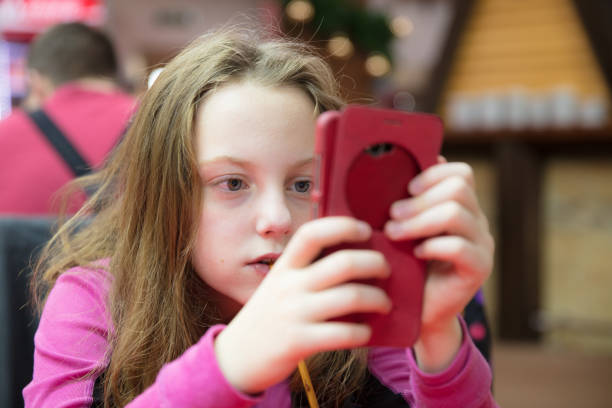Little girl sitting in a restaurant on winter vacations, using her cellphone, having fun.