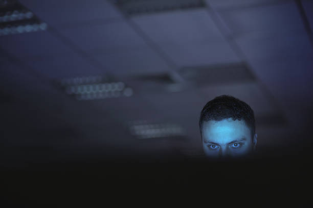 computer hacker working on laptop late at night in office - terrorism imagens e fotografias de stock