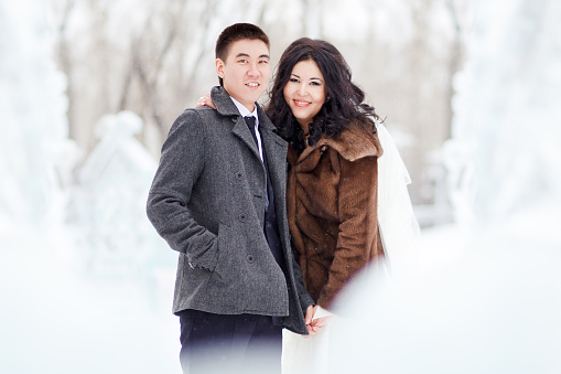 Winter wedding, the bride and groom in winter clothes on the street in the middle of snow and ice figures, looking at camera smiling.