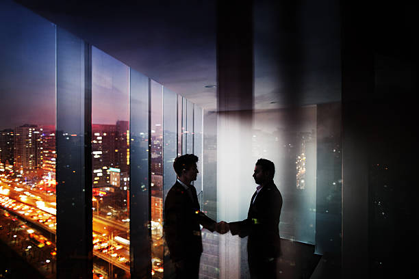 Businessmen shaking hands in office at night with city view Businessmen shaking hands in office at night with city view bribing stock pictures, royalty-free photos & images