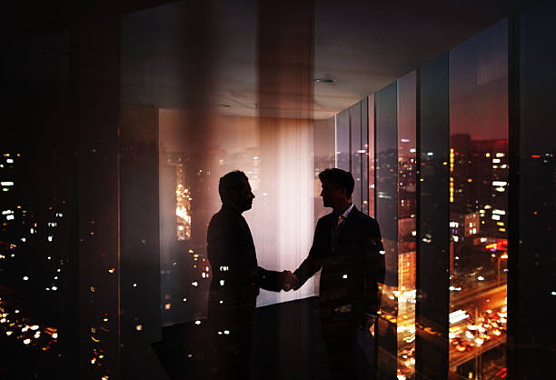 istock Businessmen shaking hands in office at night with city view 637946036