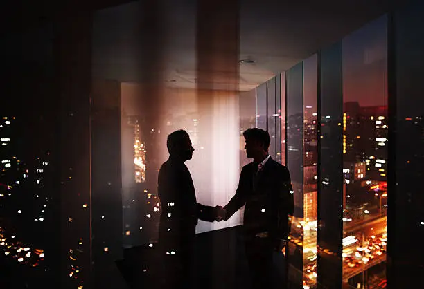 Photo of Businessmen shaking hands in office at night with city view