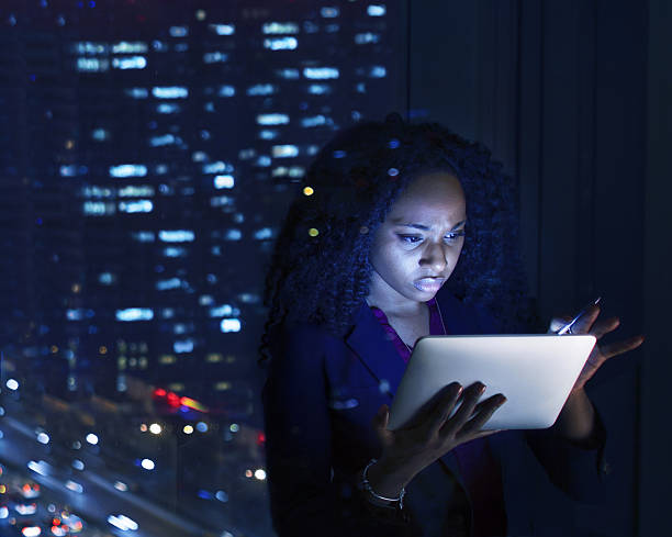 femme travaillant sur tablette la nuit au bureau - lighting equipment office building night city photos et images de collection